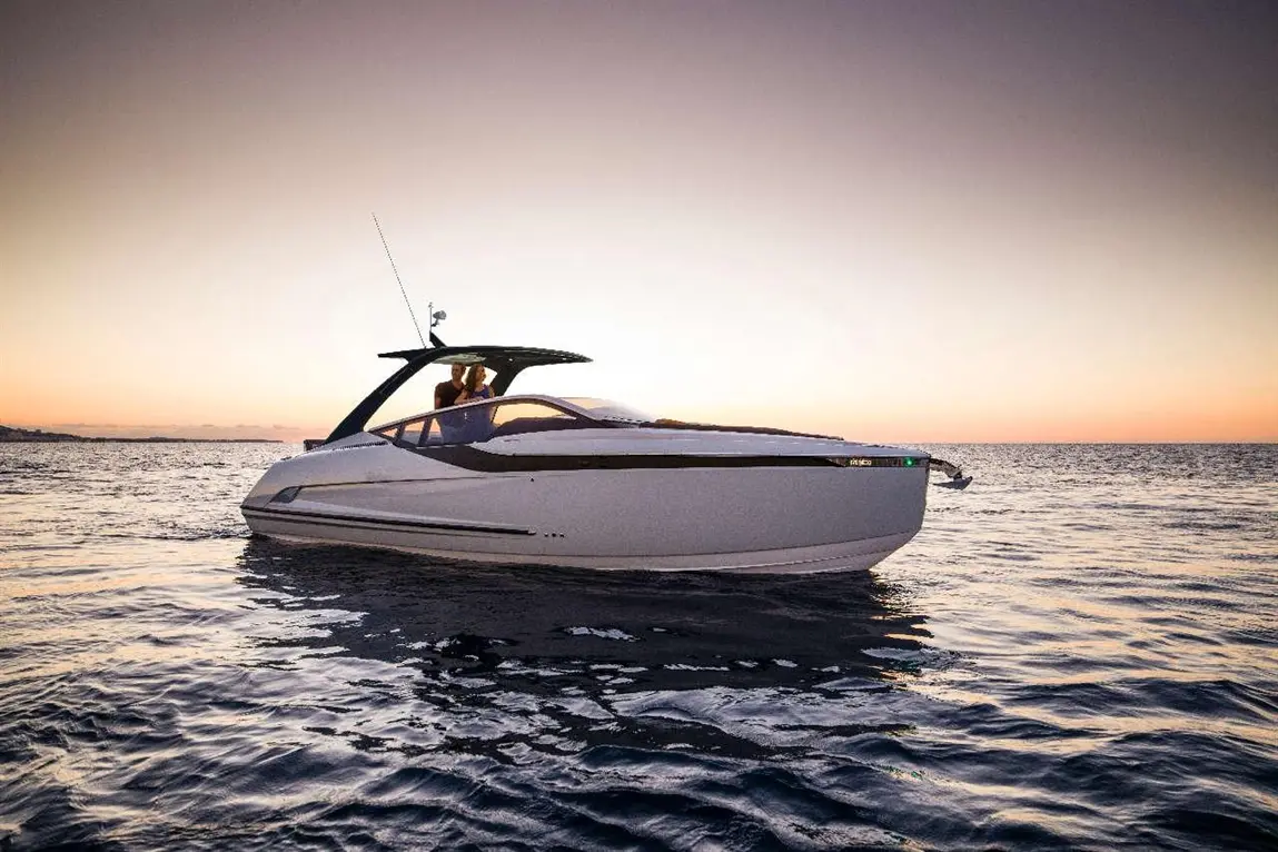Luxury motorboat at sunset with two people on board, surrounded by calm waters and a colorful sky.